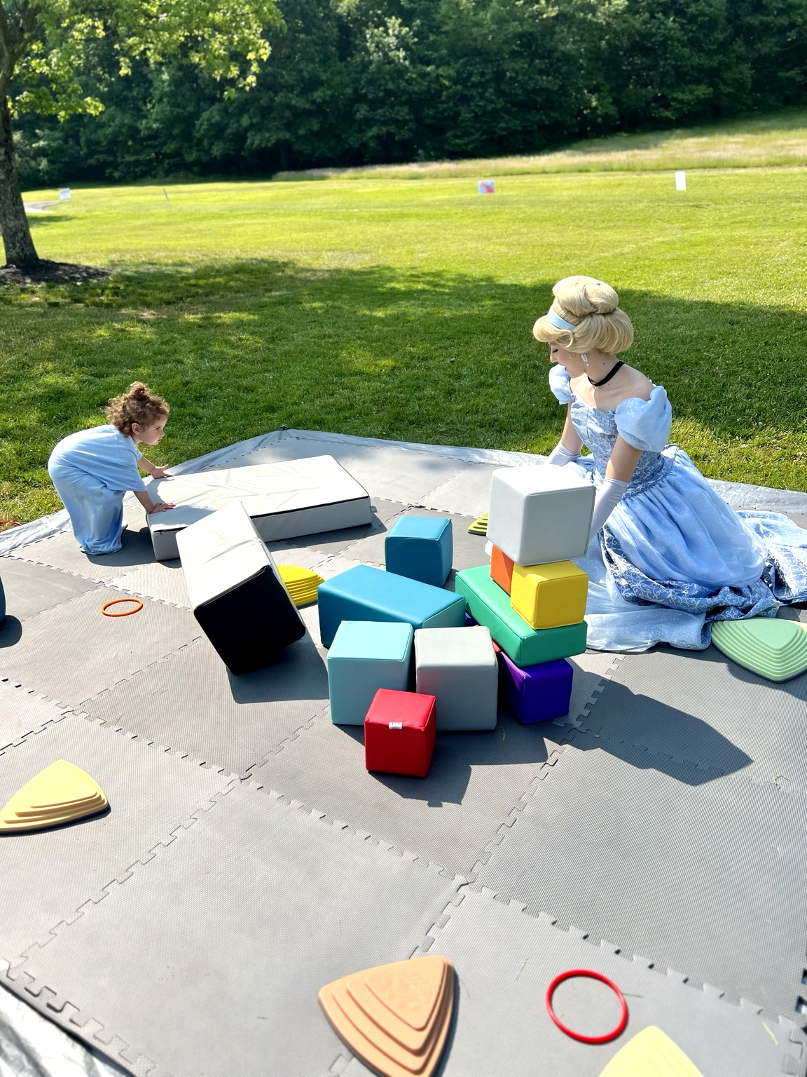 A princess character playing jumbo blocks with a toddler on the lawn