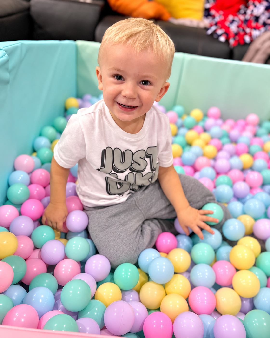 Toddler boy playing in a teal ball pit with a pastel bunting arch